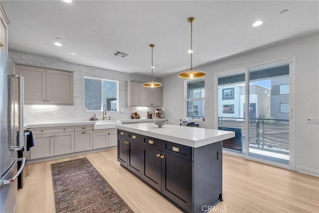 kitchen featuring tasteful backsplash, visible vents, light wood finished floors, pendant lighting, and a sink