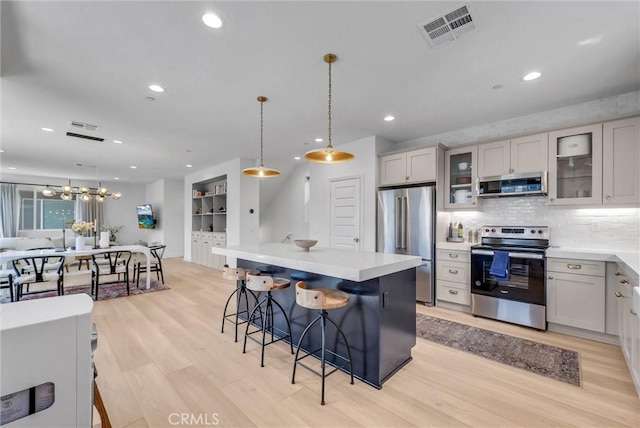 kitchen featuring visible vents, light countertops, appliances with stainless steel finishes, light wood finished floors, and a breakfast bar area