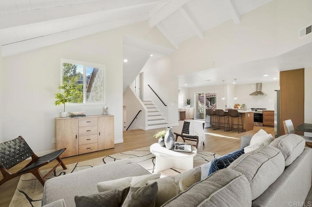 living area with beam ceiling, light wood finished floors, and stairs