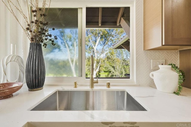 interior details with decorative backsplash, a sink, and light stone countertops