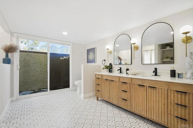 bathroom with toilet, double vanity, a sink, and baseboards