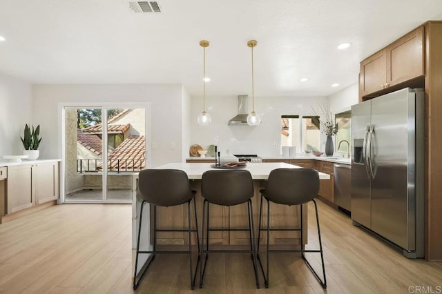 kitchen with light wood-type flooring, wall chimney range hood, visible vents, appliances with stainless steel finishes, and light countertops