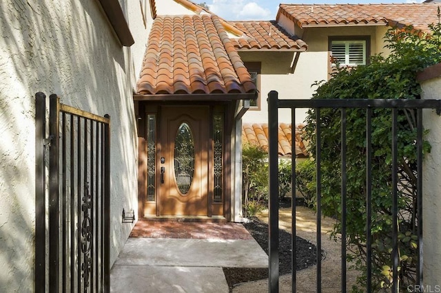 doorway to property featuring a tile roof, fence, a gate, and stucco siding