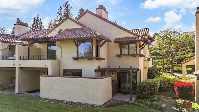 rear view of property with a tiled roof, stucco siding, a balcony, and a chimney