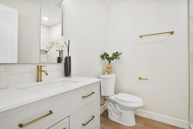 bathroom with toilet, wood finished floors, vanity, and baseboards