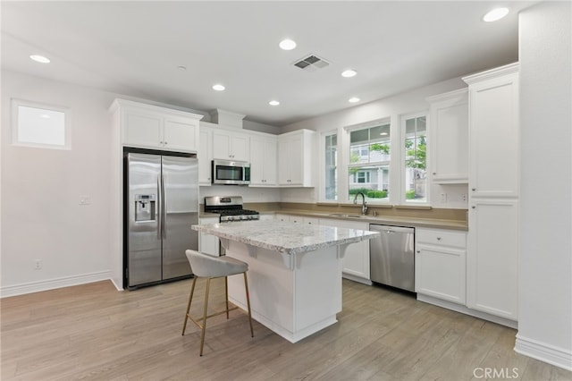 kitchen with a sink, a kitchen breakfast bar, visible vents, white cabinets, and appliances with stainless steel finishes