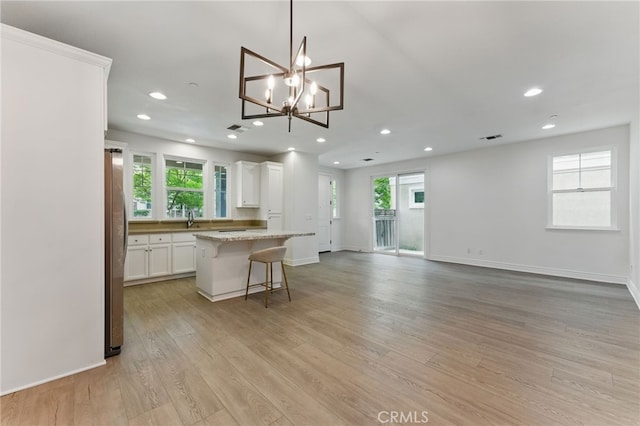 kitchen with light wood-style flooring, white cabinets, a kitchen island, freestanding refrigerator, and a kitchen bar