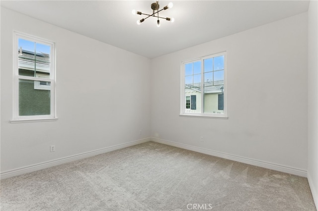 carpeted empty room with a healthy amount of sunlight, baseboards, and an inviting chandelier