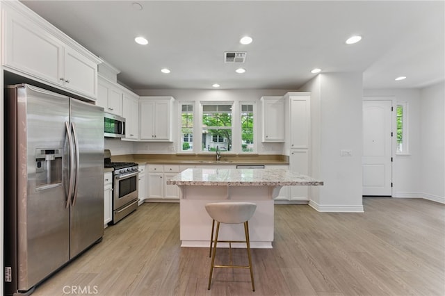 kitchen with a healthy amount of sunlight, appliances with stainless steel finishes, white cabinetry, visible vents, and a kitchen breakfast bar