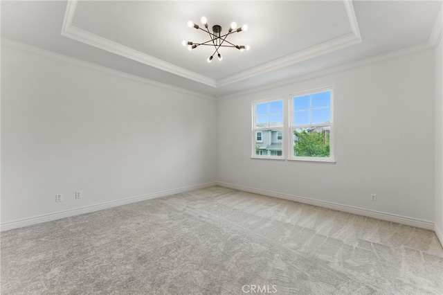 carpeted spare room featuring ornamental molding, a raised ceiling, a notable chandelier, and baseboards