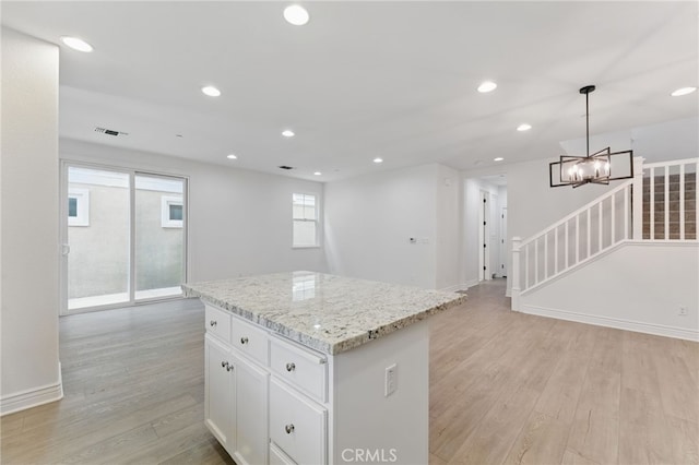 kitchen featuring white cabinetry, light wood-style flooring, a kitchen island, light stone countertops, and hanging light fixtures