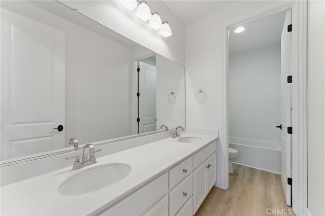 bathroom with double vanity, wood finished floors, toilet, and a sink