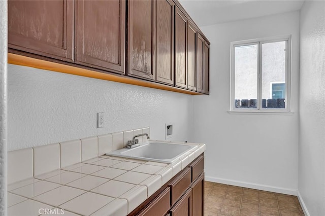 laundry area with washer hookup, a sink, a textured wall, baseboards, and cabinet space
