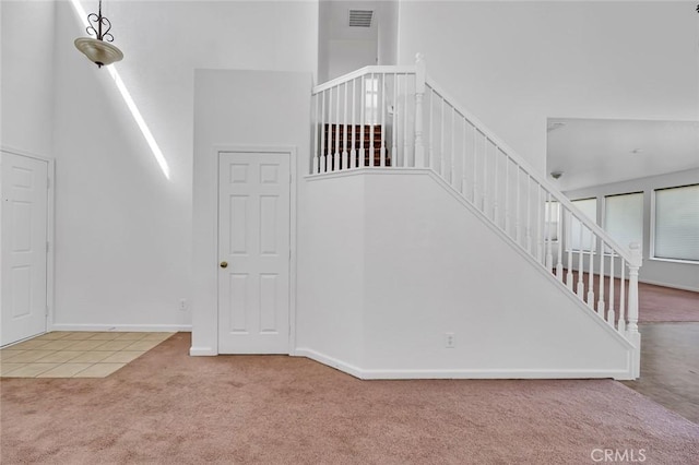 staircase with carpet flooring, visible vents, baseboards, and a towering ceiling