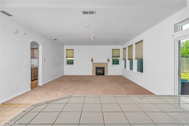 unfurnished living room with a tile fireplace, arched walkways, carpet flooring, and visible vents