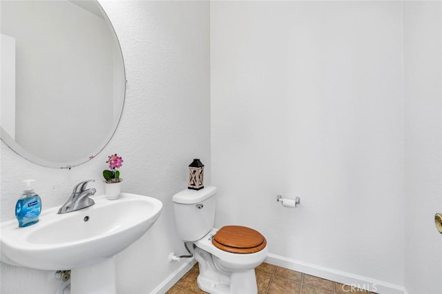 half bathroom with a sink, tile patterned floors, toilet, and baseboards