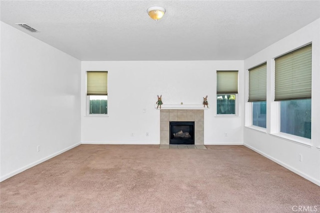 unfurnished living room featuring a tiled fireplace, visible vents, baseboards, and carpet flooring