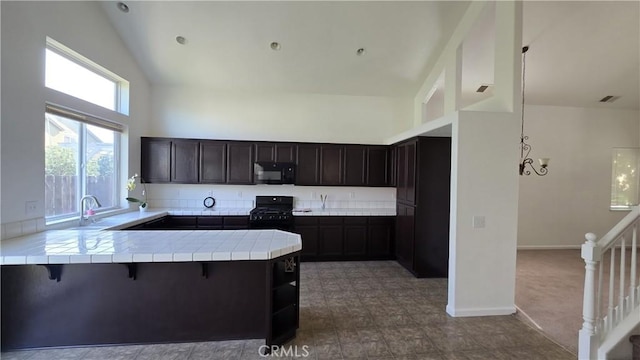 kitchen with a kitchen bar, a peninsula, tile counters, black appliances, and high vaulted ceiling
