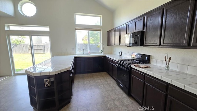 kitchen featuring a wealth of natural light, black appliances, tile countertops, and a peninsula