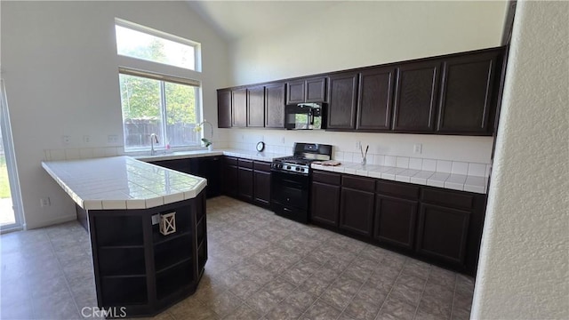 kitchen featuring tile countertops, high vaulted ceiling, a peninsula, open shelves, and range with gas stovetop