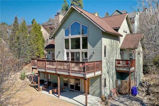 rear view of house with a patio, a deck, a chimney, and a shingled roof