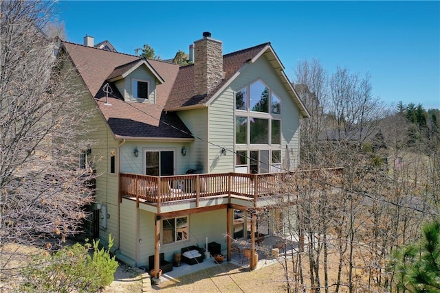 rear view of property with a patio area, roof with shingles, a wooden deck, and a chimney