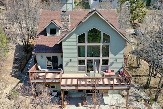 rear view of property featuring roof with shingles, a wooden deck, and a chimney