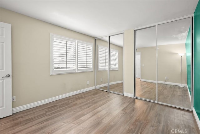 unfurnished bedroom featuring wood finished floors, baseboards, and multiple closets
