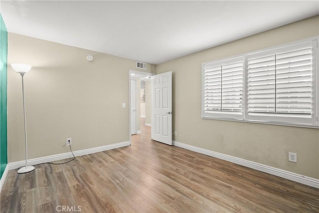 empty room featuring wood finished floors, baseboards, and visible vents