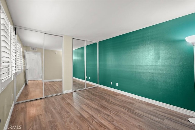 unfurnished bedroom with visible vents, baseboards, two closets, and wood finished floors