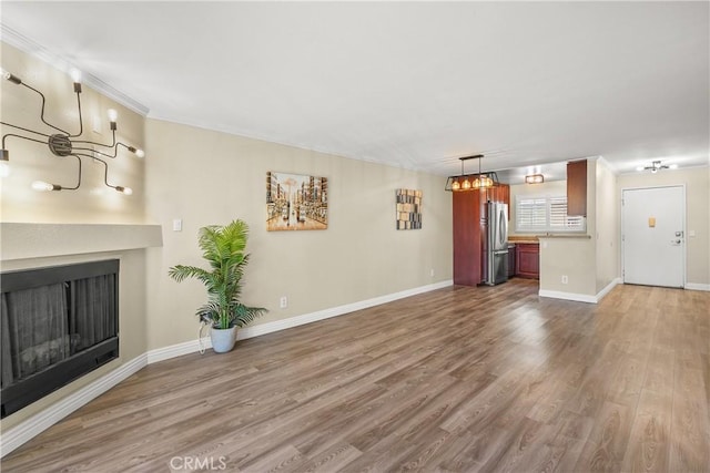 unfurnished living room with baseboards, a notable chandelier, a fireplace, crown molding, and wood finished floors