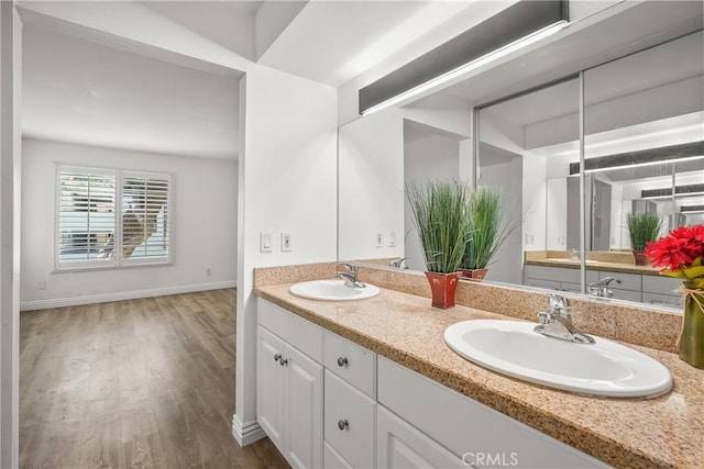 bathroom with wood finished floors, double vanity, a sink, and baseboards