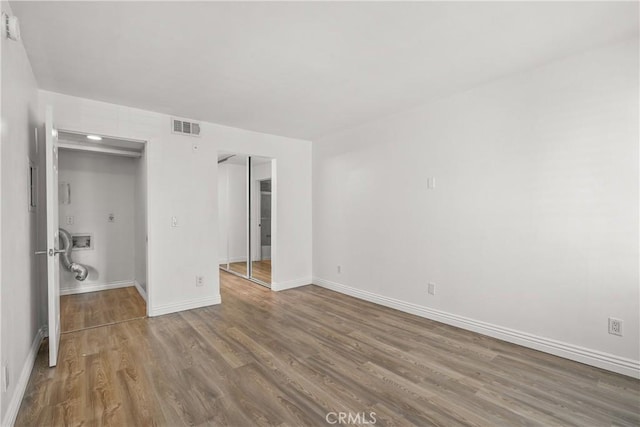 unfurnished bedroom featuring visible vents, baseboards, a walk in closet, and wood finished floors