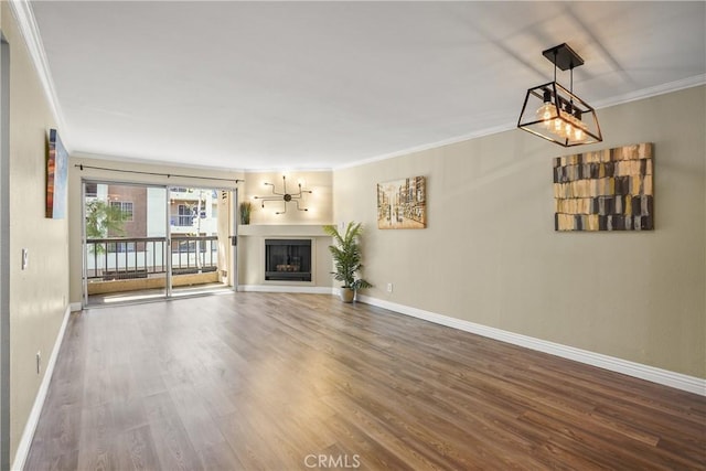 unfurnished living room with a fireplace, ornamental molding, a chandelier, wood finished floors, and baseboards