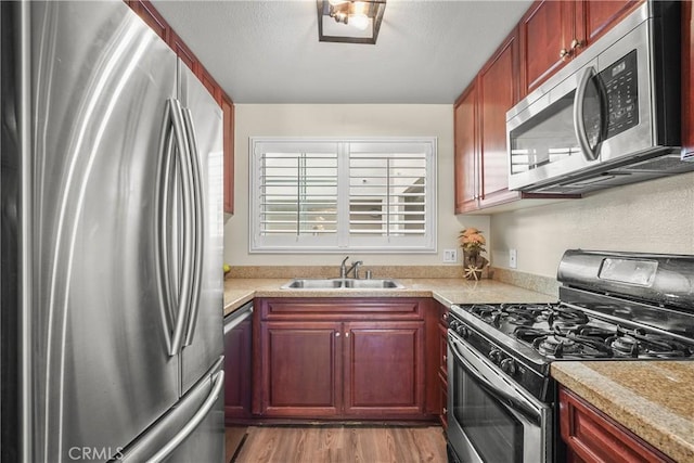 kitchen featuring stainless steel appliances, light wood-type flooring, light countertops, and a sink