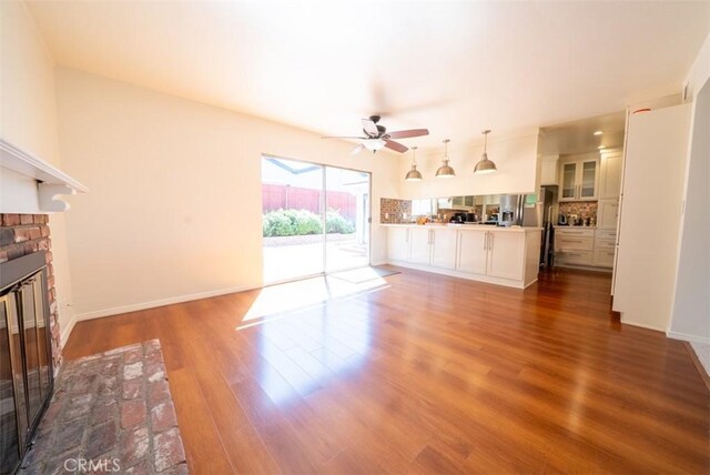 unfurnished living room featuring ceiling fan, baseboards, dark wood finished floors, and a brick fireplace