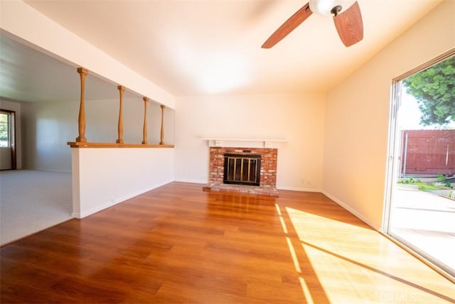 unfurnished living room featuring wood finished floors, ceiling fan, baseboards, and a brick fireplace