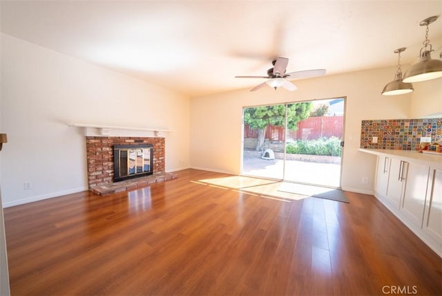 unfurnished living room featuring ceiling fan, a brick fireplace, wood finished floors, and baseboards