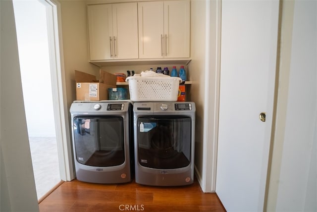 clothes washing area with independent washer and dryer, wood finished floors, and cabinet space