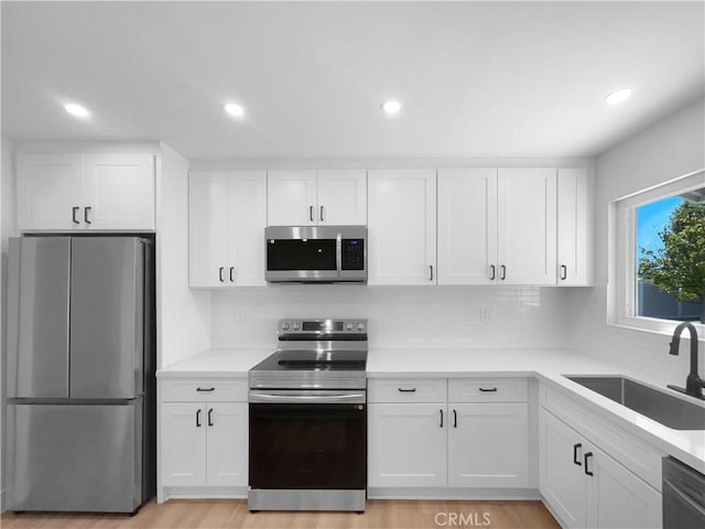 kitchen with backsplash, appliances with stainless steel finishes, a sink, and white cabinetry