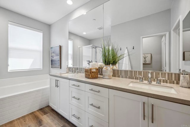 full bath featuring a bath, a stall shower, wood finished floors, and a sink