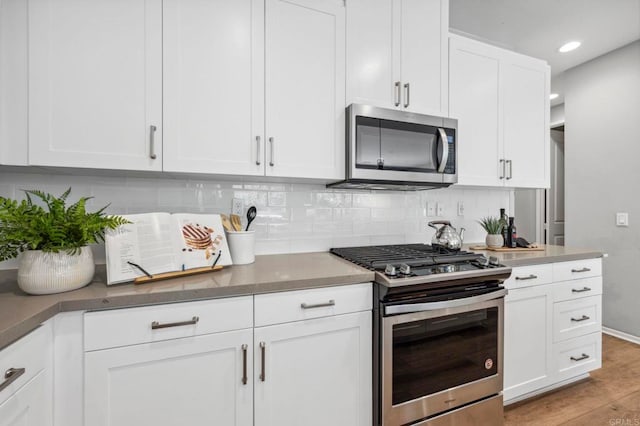 kitchen featuring stainless steel appliances, tasteful backsplash, light wood-type flooring, and white cabinetry