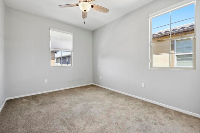 carpeted spare room featuring a healthy amount of sunlight, baseboards, and a ceiling fan