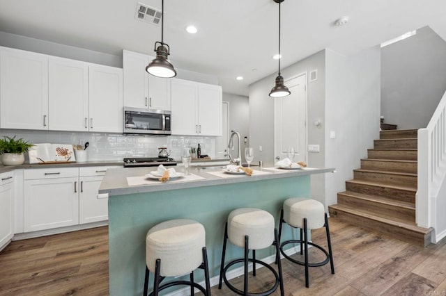 kitchen with tasteful backsplash, stainless steel microwave, a sink, a center island with sink, and dark wood-style floors