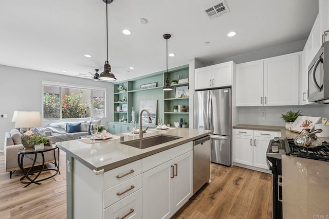kitchen with a sink, light wood-type flooring, white cabinets, and appliances with stainless steel finishes