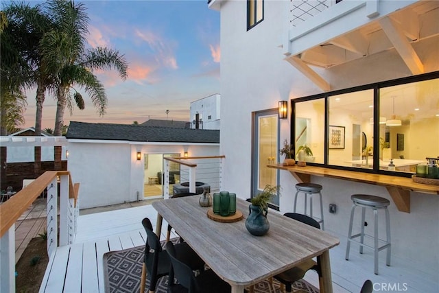 deck at dusk featuring outdoor dining space and outdoor dry bar