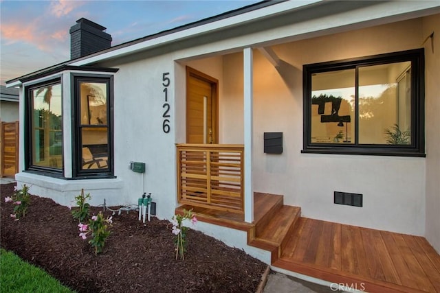 doorway to property with visible vents, a chimney, and stucco siding