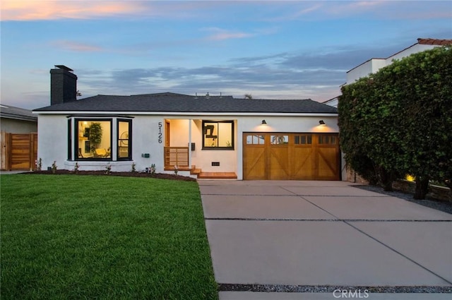 ranch-style home featuring a yard, an attached garage, a chimney, concrete driveway, and stucco siding