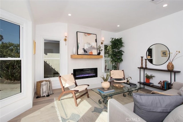 living room featuring wood finished floors, a glass covered fireplace, visible vents, and recessed lighting
