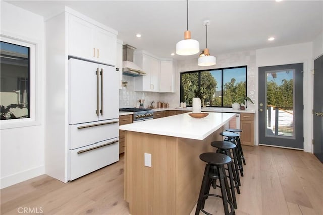 kitchen with light wood-style floors, freestanding refrigerator, wall chimney range hood, a breakfast bar, and backsplash